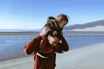 A joyful father and child bonding while walking along a sunny beach, capturing a playful moment. HD wallpaper