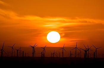 Wind turbines silhouetted against a stunning sunset, showcasing renewable energy in nature. HD wallpaper