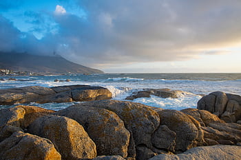 Stunning seascape view of Cape Town's rocky coastline during sunset with waves crashing against the shore. HD wallpaper