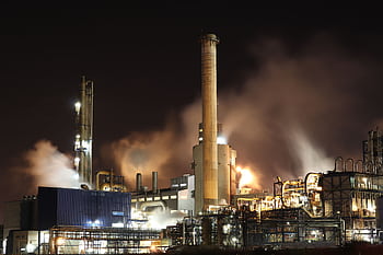 A nighttime view of an industrial factory with smokestacks emitting smoke, highlighting energy production and pollution. HD wallpaper