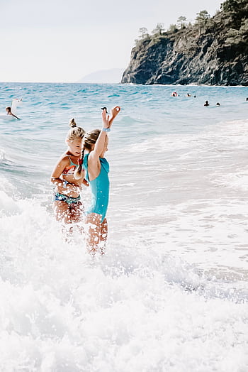 Two children having fun in ocean waves on a sunny summer beach day. HD phone wallpaper