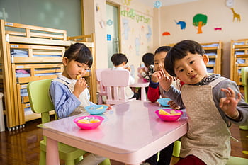 Kids seated around a table in a colorful classroom, eating snacks happily. HD wallpaper