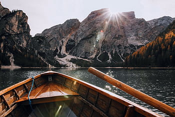 Wooden boat sailing on a serene mountain lake with sunrays illuminating the scenic landscape. HD wallpaper