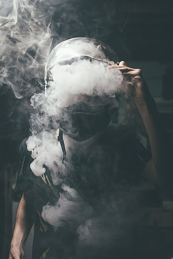 Dramatic portrait of a man wearing a motorcycle helmet surrounded by vape smoke in a dark setting. HD phone wallpaper