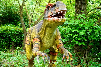 A realistic dinosaur statue in a tranquil forest, surrounded by lush greenery and trees. HD wallpaper