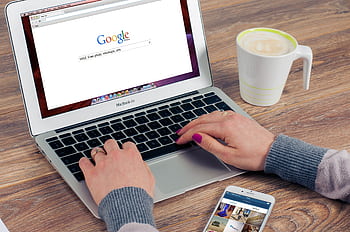 Hands typing on MacBook Air with Google search open, coffee nearby. HD wallpaper