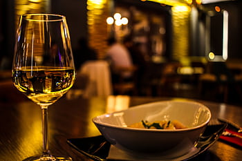 A classy dining setup featuring a glass of white wine in a cozy restaurant setting. HD wallpaper