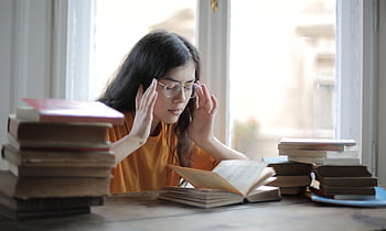 A young woman feeling fatigued while reading and studying surrounded by books. HD wallpaper