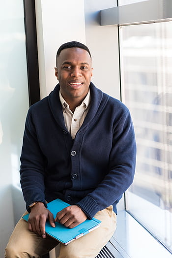 A professional black man smiling while seated by a window, embodying modern business vibes. HD phone wallpaper