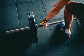 Close-up of a person lifting a barbell in an indoor gym, focusing on strength training. HD wallpaper