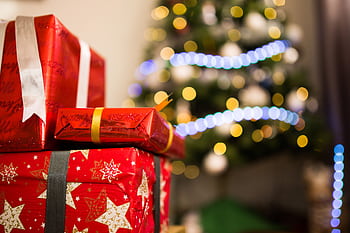 Christmas presents in red wrapping with a glowing bokeh tree background, emphasizing holiday spirit. HD wallpaper