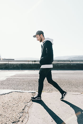 Casual male in a cap and hoodie walks along a sunny urban street. HD phone wallpaper