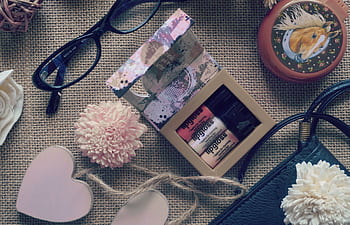 Creative flat lay composition featuring lip gloss, eyewear, flowers, and a purse on burlap for a chic look. HD wallpaper