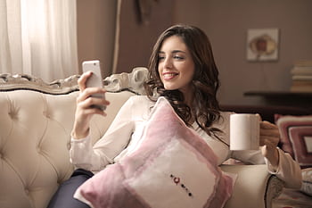 A young woman relaxing on a sofa, enjoying coffee and using her smart indoors. HD wallpaper
