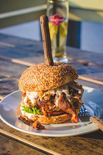 Delicious gourmet burger packed with bacon, cheese, and sauce on a sunny day. HD phone wallpaper