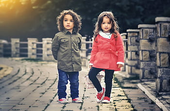 Adorable siblings smiling outdoors in colorful outfits on a sunny day. HD wallpaper