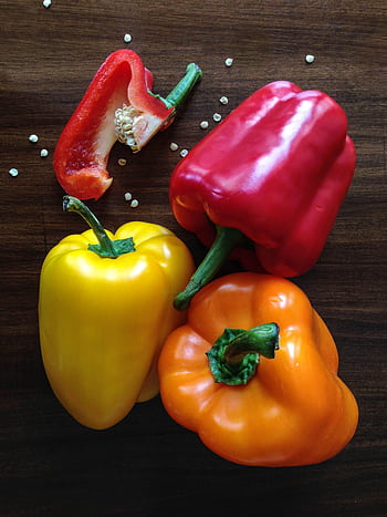 Three vibrant bell peppers on a wooden surface, perfect for cooking inspiration. HD phone wallpaper
