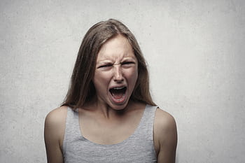 A woman with an intense facial expression screaming against a neutral gray background. HD wallpaper