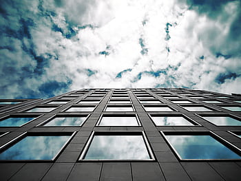 Low angle of a modern skyscraper reflecting clouds in its glass windows with a dramatic sky. HD wallpaper