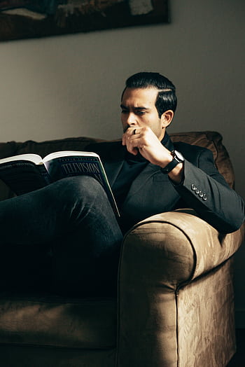 A well-dressed man thoughtfully reading a book indoors, exuding confidence and intelligence. HD phone wallpaper