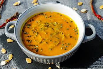 Warm and creamy pumpkin soup garnished with fresh herbs, perfect for a cozy meal. HD wallpaper