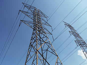 Low angle view of towering electrical transmission lines and pylons under a clear blue sky, conveying energy and electricity concepts. HD wallpaper