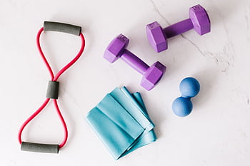 Colorful home workout equipment, including dumbbells and resistance bands, on a marble surface. HD wallpaper