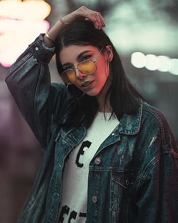 Fashionable woman posing confidently with sunglasses and denim jacket during a night shoot. HD phone wallpaper
