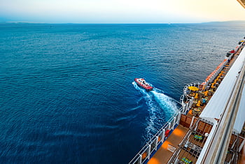 Aerial view of a luxury cruise ship with a small boat on a vast ocean at sunset. HD wallpaper