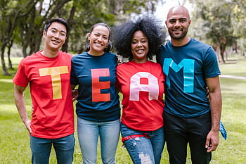 A diverse group of adults bonding and smiling in a park wearing TEAM shirts. HD wallpaper