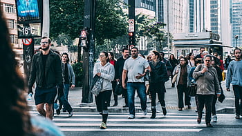 A diverse group of people crossing a street in a bustling city setting with skyscrapers. HD wallpaper
