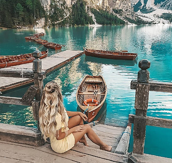 ANDREANE CHAMBERLAND, platinum blonde, brunette, collection of boats, yellow mini dress, trees, sitting by boat dock, high mountains HD wallpaper