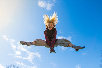 A girl energetically jumping under a clear blue sky, expressing dom and joy. HD wallpaper