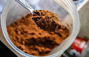 Focused shot of a spoon scooping cocoa powder from a container, emphasizing texture. HD wallpaper