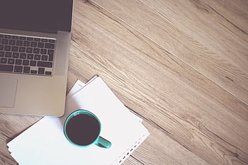 A minimalist workspace featuring a coffee cup, laptop, and wooden desk, offering a productive and stylish environment. HD wallpaper