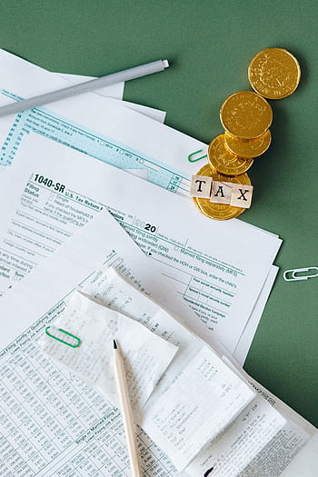 Tax documents and gold coins on a green desk symbolizing financial planning and savings. HD phone wallpaper