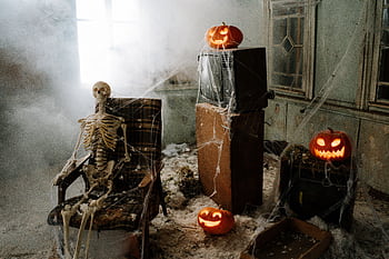 Eerie room with a skeleton, jack-o'-lanterns, cobwebs, and fog for a haunting Halloween vibe. HD wallpaper