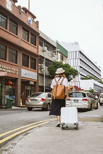 A woman with a suitcase and backpack walks down a busy city street on a sunny day. HD phone wallpaper