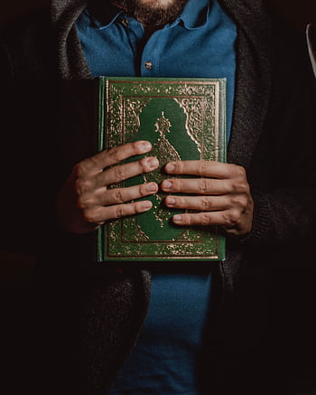 A person holds a Quran, showcasing its intricate cover, symbolizing reverence and religious devotion. HD phone wallpaper
