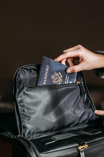 Close-up of a person placing a passport into a leather bag, ready for travel. HD phone wallpaper
