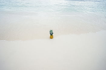 A vibrant pineapple rests on the sandy beach, with gentle waves approaching in a tranquil seaside setting. HD wallpaper