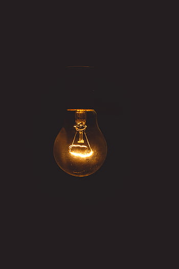 A glowing incandescent lightbulb illuminates a dark setting, symbolizing energy and innovation. HD phone wallpaper