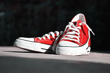 Close-up of vibrant red canvas sneakers with white laces on an outdoor surface. HD wallpaper