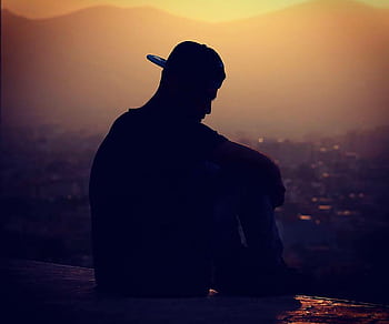 A silhouetted man in cap sits thoughtfully against a sunset background. HD wallpaper