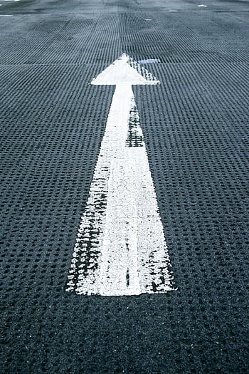 Close-up of a white directional arrow on a textured asphalt road, symbolizing forward movement and guidance. HD phone wallpaper