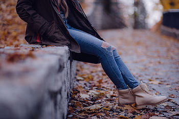 Woman wearing a jacket and boots sits casually on a fall leaf-strewn path in a relaxed mood. HD wallpaper