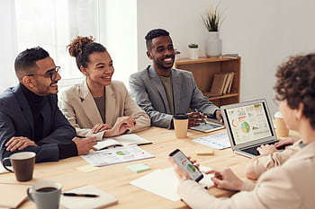Young professionals discussing work at a conference table with technology and documents. HD wallpaper