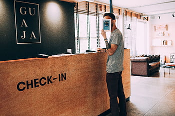 Man standing at a reception desk, holding a book, in a modern hotel lobby. HD wallpaper