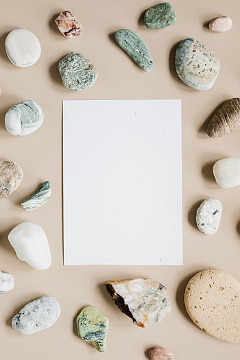 Flat lay of assorted rocks framing a blank paper sheet on a beige surface. HD phone wallpaper