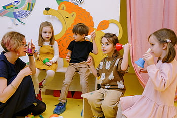 Young children playing musical bells in a colorful classroom setting with a teacher. HD wallpaper